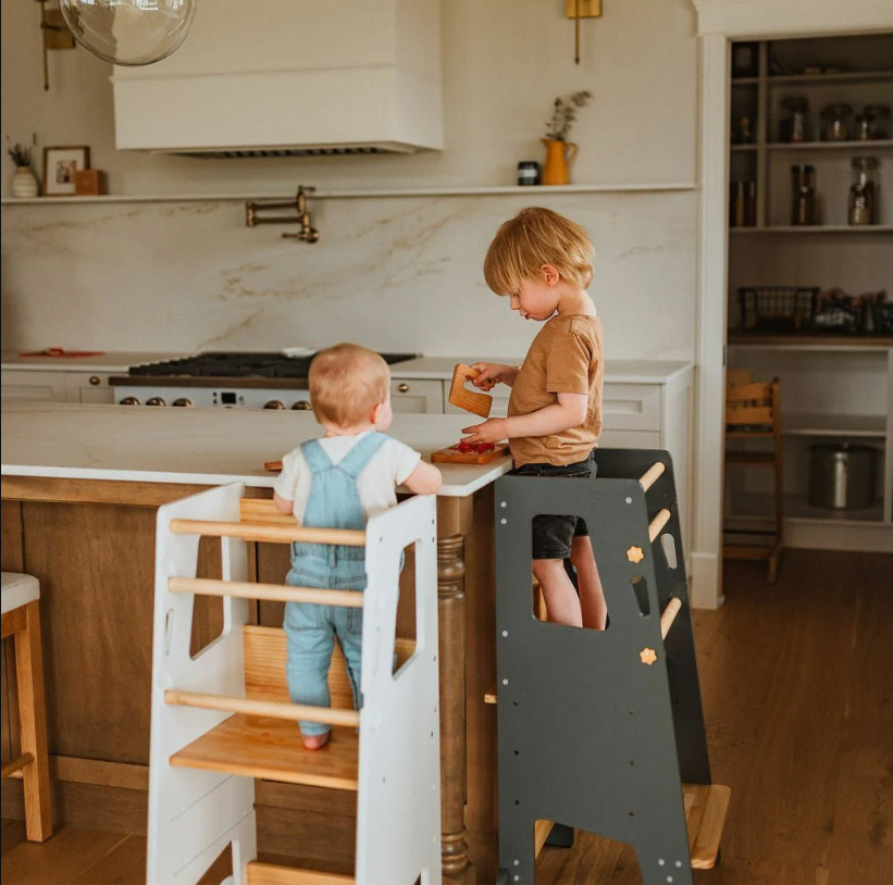 Kind steht sicher auf einem Montessori Lernturm in der Küche
