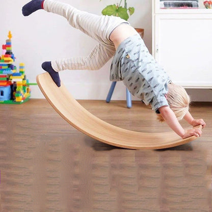 Ein Junge macht einen Handstand auf einem natürlichen Holz-Wackelbrett im Innenbereich.