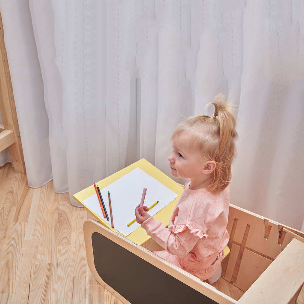 Montessori Lernturm aus Naturholz mit gelbem seitlichem Busy Board, ausgestattet mit interaktiven Zahnrädern, Schiebereglern und verschließbaren Elementen für Kleinkinder.
