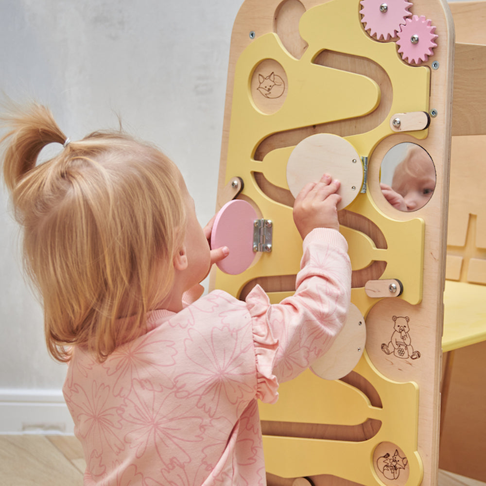 Montessori Lernturm aus Naturholz mit gelbem seitlichem Busy Board, ausgestattet mit interaktiven Zahnrädern, Schiebereglern und verschließbaren Elementen für Kleinkinder.